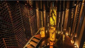 A luxurious wine cellar with walls lined with bottles. Two tall, illuminated columns and a spiral staircase are featured, creating a warm, elegant atmosphere—a true example of the latest renovation trends. Personalized Wine Cellars like this one are becoming increasingly popular as standout reno trends in Canada.