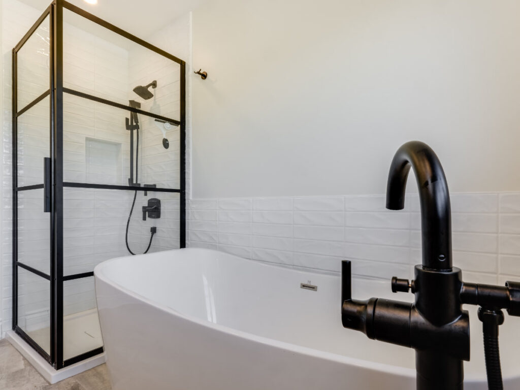 Modern bathroom with a white freestanding bathtub, black faucet, and a glass shower with black frame. The walls have white textured tiles and the floor appears light-colored—an elegant design often found in today’s net zero ready homes, where energy efficiency meets contemporary style.