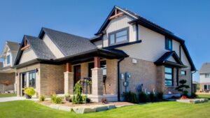 A modern two-story suburban house with light brick and beige siding, black trim, large windows, and a well-kept front lawn with landscaping, under a clear blue sky—this home exemplifies the next generation of Net Zero Homes, offering outstanding energy efficiency incentives for sustainable living.