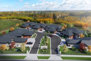 Aerial view of a small, modern residential community with net zero homes arranged around a circular road, surrounded by green lawns, trees, and a forested area in the background.