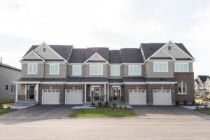 A row of modern two-story townhouses with attached garages, front lawns, and large windows, set in a residential neighborhood on a sunny day—beautiful examples of net zero homes designed to support sustainable living within vibrant net zero communities.