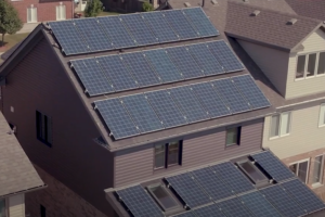 A house with multiple rows of solar panels installed on its roof, surrounded by other houses in a residential neighborhood, exemplifies the innovative approach of net zero homes that are increasingly popular in net zero communities.