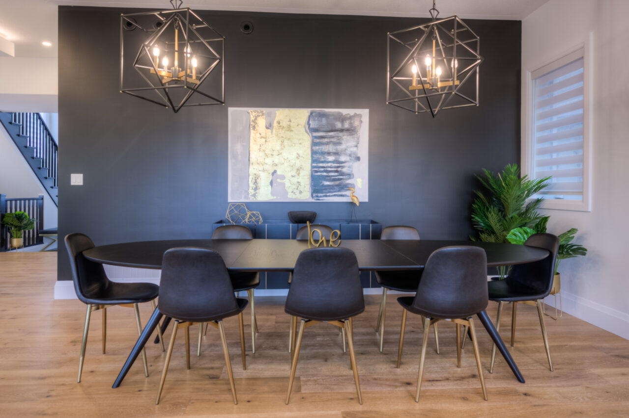 Modern dining room with a black oval table, eight black chairs with gold legs, geometric pendant lights, abstract wall art, a love decor piece on the table, and green plants on hardwood floors—perfectly suited for stylish net zero homes that blend sustainability with contemporary elegance.