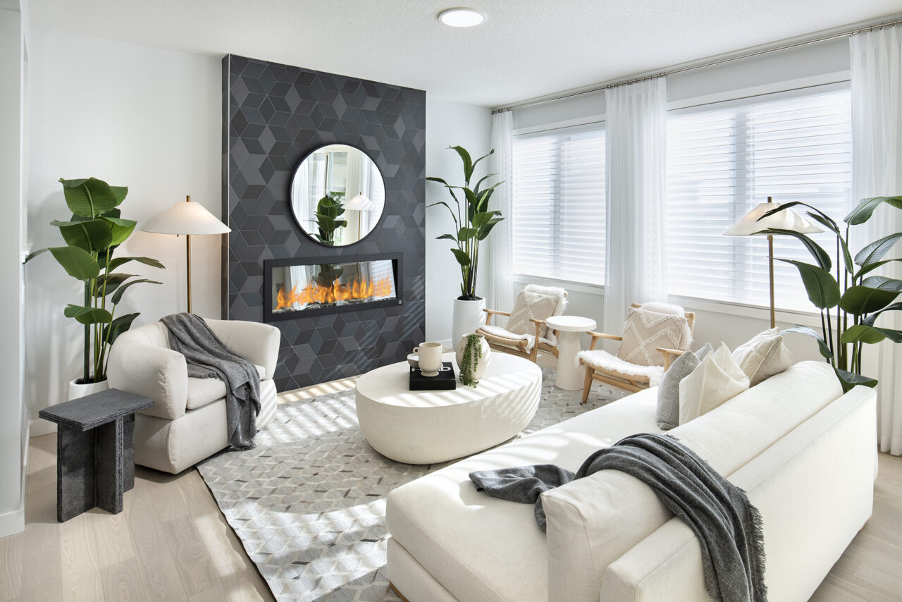 Modern living room with white sofas, a geometric black fireplace, a round mirror, greenery, and large windows with sheer curtains. Neutral tones and cozy decor create a bright, inviting space—perfect for those seeking the comfort and sustainability found in net zero homes.