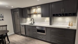 Modern kitchen with grey cabinets, stainless steel appliances, and a wine rack—perfect for adaptiv home renovations or multi-generational living. Decorative items adorn the counters, and a round dining table is partially visible.