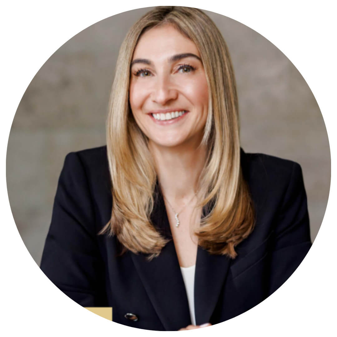 A woman with long, straight blonde hair and a black blazer smiles while seated in front of a neutral background.