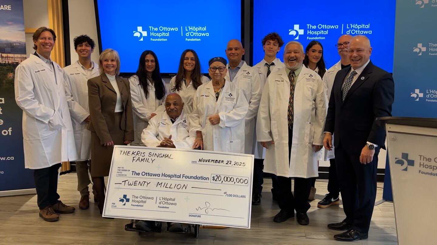 A group of people in lab coats and formal attire pose with a giant $20 million check from the Singhal family to The Ottawa Hospital Foundation. Two people stand behind the check, while others—including representatives from Richcraft Homes—stand smiling around them.
