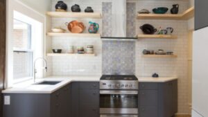 Modern kitchen with dark cabinets, open wooden shelves displaying pottery, a stainless steel stove, patterned tile backsplash, white subway tile walls, and a large window above the sink.