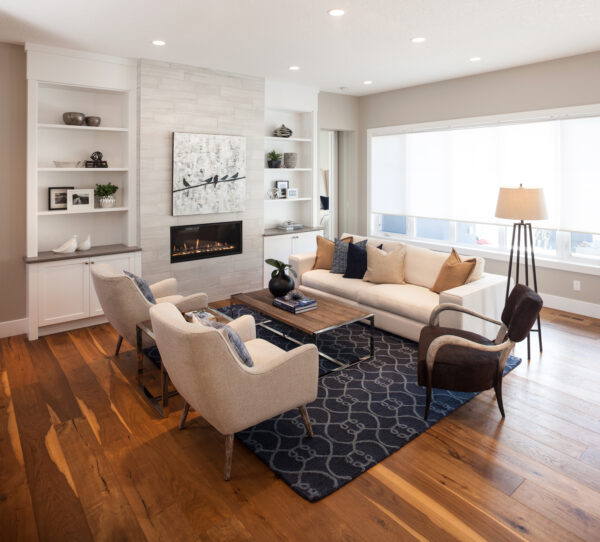 Modern living room with fabulous flooring, a white sofa, two beige chairs, a black armchair, a blue patterned rug, a floor lamp, built-in shelves, and a fireplace with art above it. Large windows let in natural light—perfect inspiration for your next home renovation.