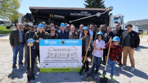 A group of people, including children in blue hard hats, pose with shovels in front of a truck at a Habitat for Humanity Niagara groundbreaking event. A sign announces the construction coming in Spring 2024.