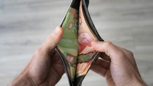 A person holds an open wallet containing several Canadian banknotes in various denominations, viewed from above against a light-colored wooden floor background.