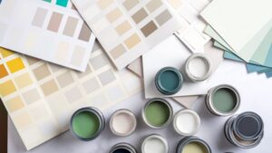Multiple open paint cans in shades of green, blue, and neutral colors are surrounded by several paint swatch cards displaying a variety of color options on a light surface.