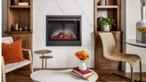 Modern living room with an electric fireplace, two wooden shelves, a woven chair, a round white coffee table with flowers and books, and a small round glass dining table with a white vase.