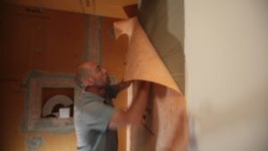 A person applies a large sheet of waterproofing membrane to a bathroom wall during a renovation project.